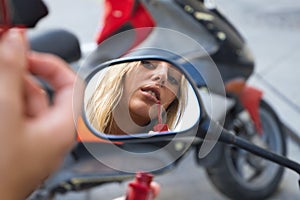 A beautiful blonde woman sits on a red motorbike that she has rented for her holiday in the tourist town. The girl is wearing a