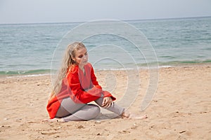 Beautiful blonde woman sits on the sand on an empty beach by the sea