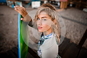 Beautiful blonde woman sits on wooden pier and holds wakesurf board with her hand photo