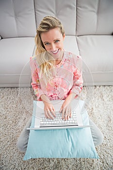 Beautiful blonde woman sitting on the floor using laptop