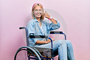 Beautiful blonde woman sitting on wheelchair pointing with hand finger to face and nose, smiling cheerful