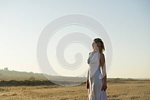 Beautiful blonde woman in slinky white dress posing in field of golden grass
