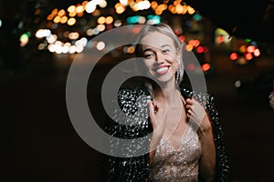 Beautiful blonde woman smiling looking at camera outdoors at night city lights street