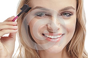 Beautiful blonde woman smiling while using eyebrows comb