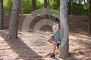 Beautiful blonde woman with straight hair is dressed in brown top and short denim skirt and hat. The woman is happy and leans