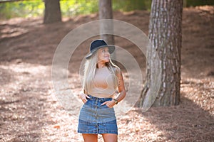 Beautiful blonde woman with straight hair is dressed in brown top and short denim skirt and hat. The woman is happy and walks