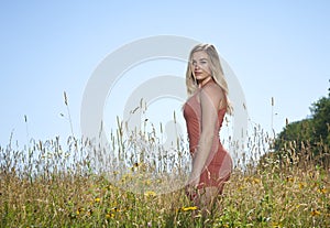 Beautiful blonde woman summer fashion outdoors in field of flowers and tall grass