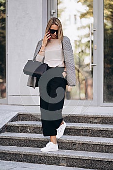 Beautiful blonde woman talking on phone walking on street.Portrait of stylish smiling business woman in Dark casual
