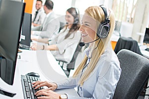 Beautiful blonde woman telephone operator talking with customer in call center.