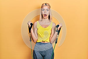 Beautiful blonde woman training arm resistance with elastic arm bands afraid and shocked with surprise and amazed expression, fear