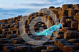 Beautiful blonde woman in turquoise long dress at Giants Causeway in North Ireland