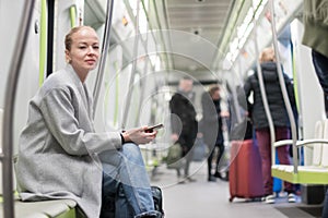 Beautiful blonde woman using smart phone while traveling by metro public transport.