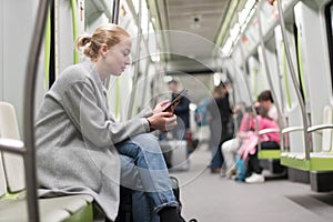 Beautiful blonde woman using smart phone while traveling by metro public transport.