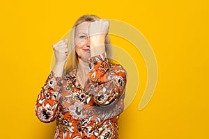 Beautiful blonde woman on vacation in patterned dress on yellow background. Ready to fight with fist defense gesture