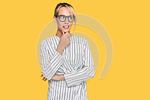 Beautiful blonde woman wearing business shirt and glasses with hand on chin thinking about question, pensive expression