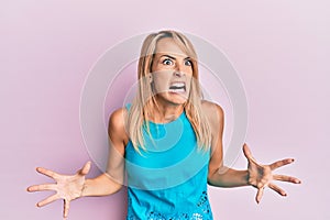 Beautiful blonde woman wearing casual clothes crazy and mad shouting and yelling with aggressive expression and arms raised