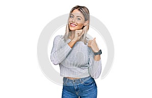 Beautiful blonde woman wearing casual clothes pointing to the back behind with hand and thumbs up, smiling confident