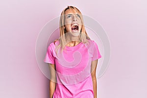 Beautiful blonde woman wearing casual pink tshirt angry and mad screaming frustrated and furious, shouting with anger