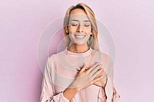 Beautiful blonde woman wearing casual winter sweater smiling with hands on chest with closed eyes and grateful gesture on face