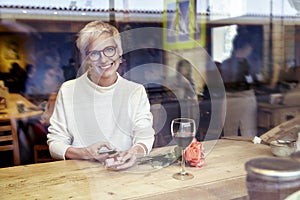 Beautiful blonde woman wearing eyeglasses looking to camera, using mobile phone in cafe. Got a love message.