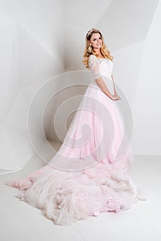Beautiful blonde woman wearing gorgeous long dress and crystal crown posing in studio on white polygonal background