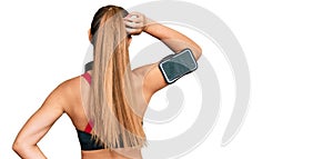 Beautiful blonde woman wearing gym clothes and using headphones backwards thinking about doubt with hand on head