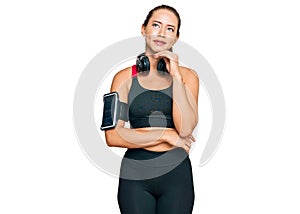 Beautiful blonde woman wearing gym clothes and using headphones with hand on chin thinking about question, pensive expression