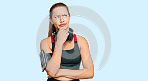 Beautiful blonde woman wearing gym clothes and using headphones thinking worried about a question, concerned and nervous with hand