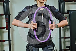 Beautiful blonde woman wearing in sensors and belts, fastens with velcro is practicing EMS fitness in a gym, building up