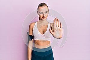 Beautiful blonde woman wearing sportswear and arm band doing stop sing with palm of the hand