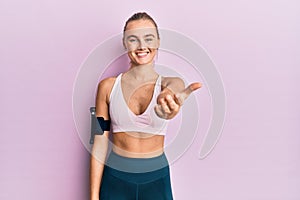 Beautiful blonde woman wearing sportswear and arm band smiling friendly offering handshake as greeting and welcoming