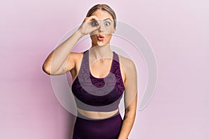 Beautiful blonde woman wearing sportswear over pink background doing ok gesture shocked with surprised face, eye looking through