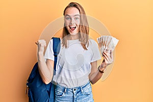 Beautiful blonde woman wearing student backpack and holding 5000 south korean won pointing thumb up to the side smiling happy with