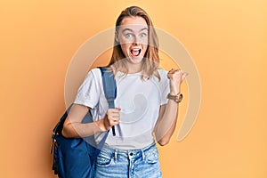 Beautiful blonde woman wearing student backpack pointing thumb up to the side smiling happy with open mouth