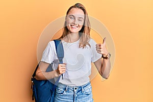 Beautiful blonde woman wearing student backpack smiling happy and positive, thumb up doing excellent and approval sign
