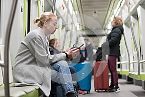 Beautiful blonde woman wearing winter coat reading on the phone while traveling by metro public transport.