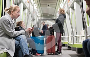 Beautiful blonde woman wearing winter coat reading on the phone while traveling by metro public transport.