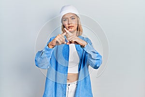 Beautiful blonde woman wearing wool hat rejection expression crossing fingers doing negative sign
