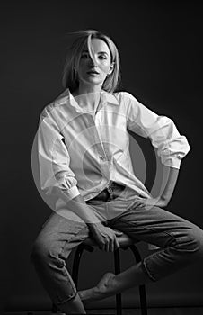 Beautiful blonde woman in a white shirt posing in the studio on a black background. Black and white photo. Model Tests