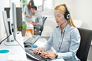 Beautiful blonde young business woman with headset using computer at office.