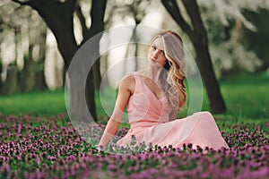 Beautiful blonde young woman in colorful flowers. girl with make-up and hairstyle in pink dress in blossoming spring park. woman`