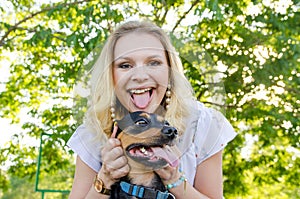 A beautiful blonde young woman and a dog have fun together and show their tongues