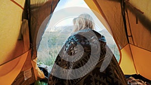 Beautiful blonde young woman enter in the tent camping just on big mountain. The concept of freedom in solitude among