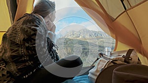 Beautiful blonde young woman enter in the tent camping just on big mountain. The concept of freedom in solitude among