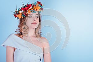 Beautiful Blonde Young Woman with Flowers Wreath, Long Curly Hair and Makeup on Blue Background