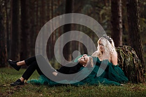 A beautiful blonde young woman in a long green dress and a diadem on her head with stylish young son in the forest. girl and boy