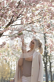 Beautiful blonde young woman in Sakura Cherry Blossom park in Spring enjoying nature and free time during her traveling