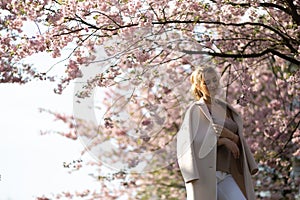 Beautiful blonde young woman in Sakura Cherry Blossom park in Spring enjoying nature and free time during her traveling