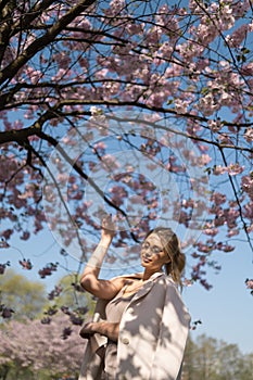 Beautiful blonde young woman in Sakura Cherry Blossom park in Spring enjoying nature and free time during her traveling