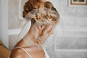 Beautiful blonde young woman with stylish wedding hairstyle in fashionable white lace lingerie posing at vintage